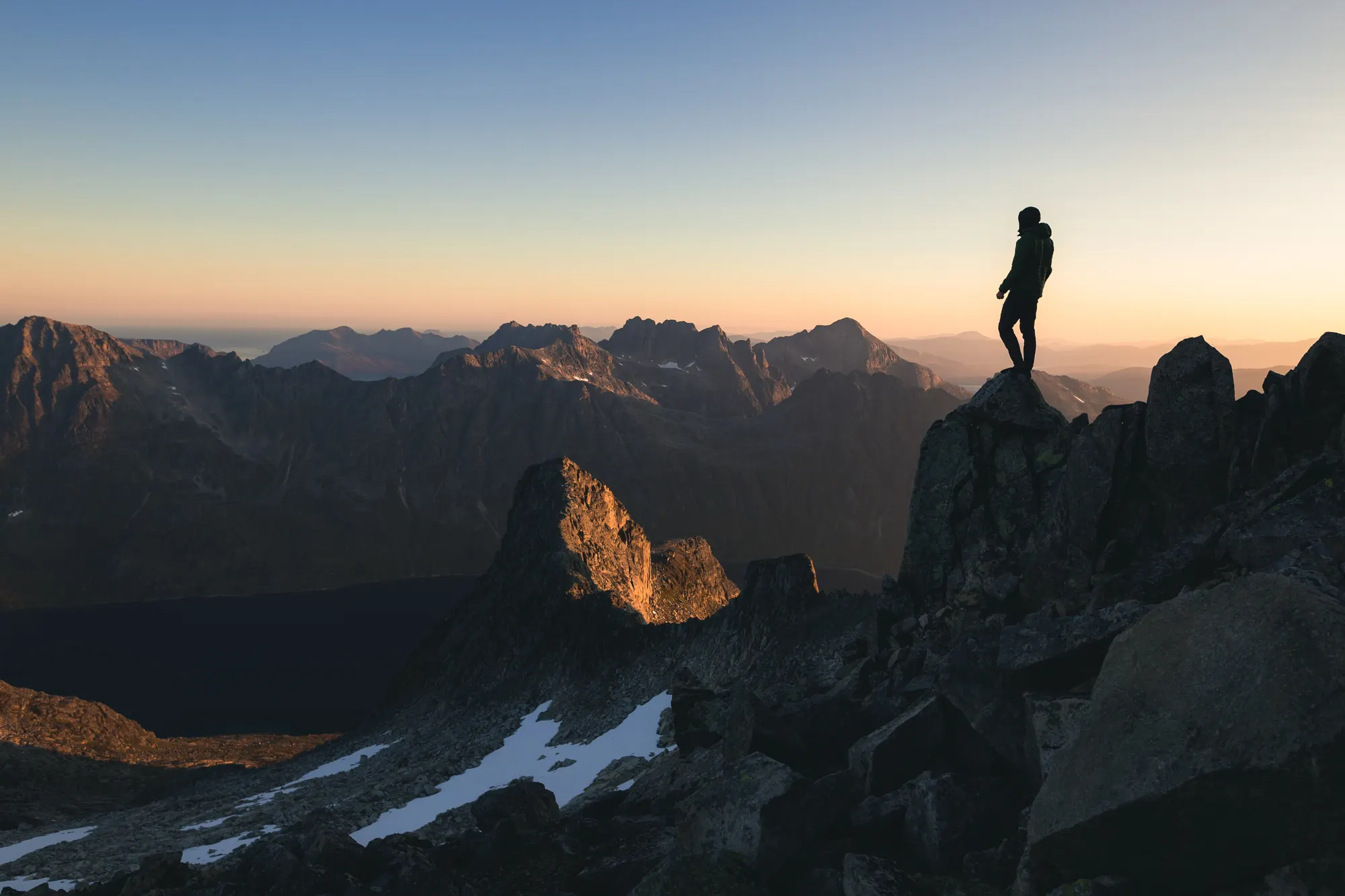 Silhouette of a person standing on a mountain ridge at sunrise, overlooking a range of peaks
